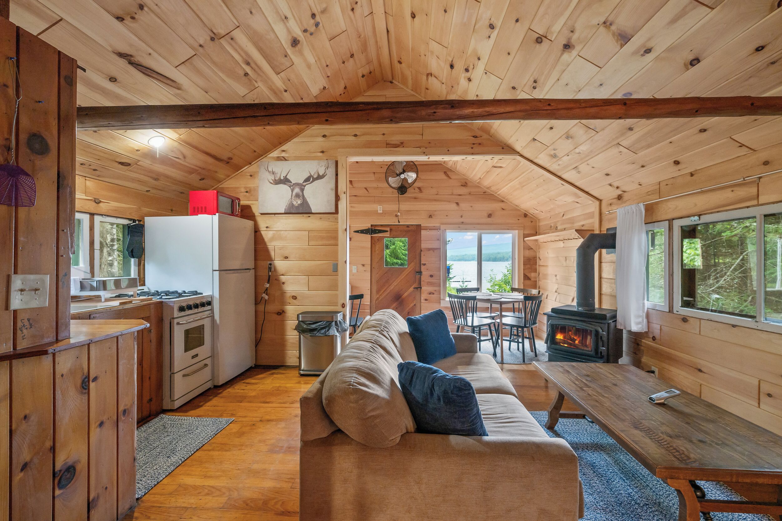 Un intérieur de chalet chaleureux, avec un revêtement mural en bois, un coin cuisine équipé d’une cuisinière, un canapé et une table à manger.