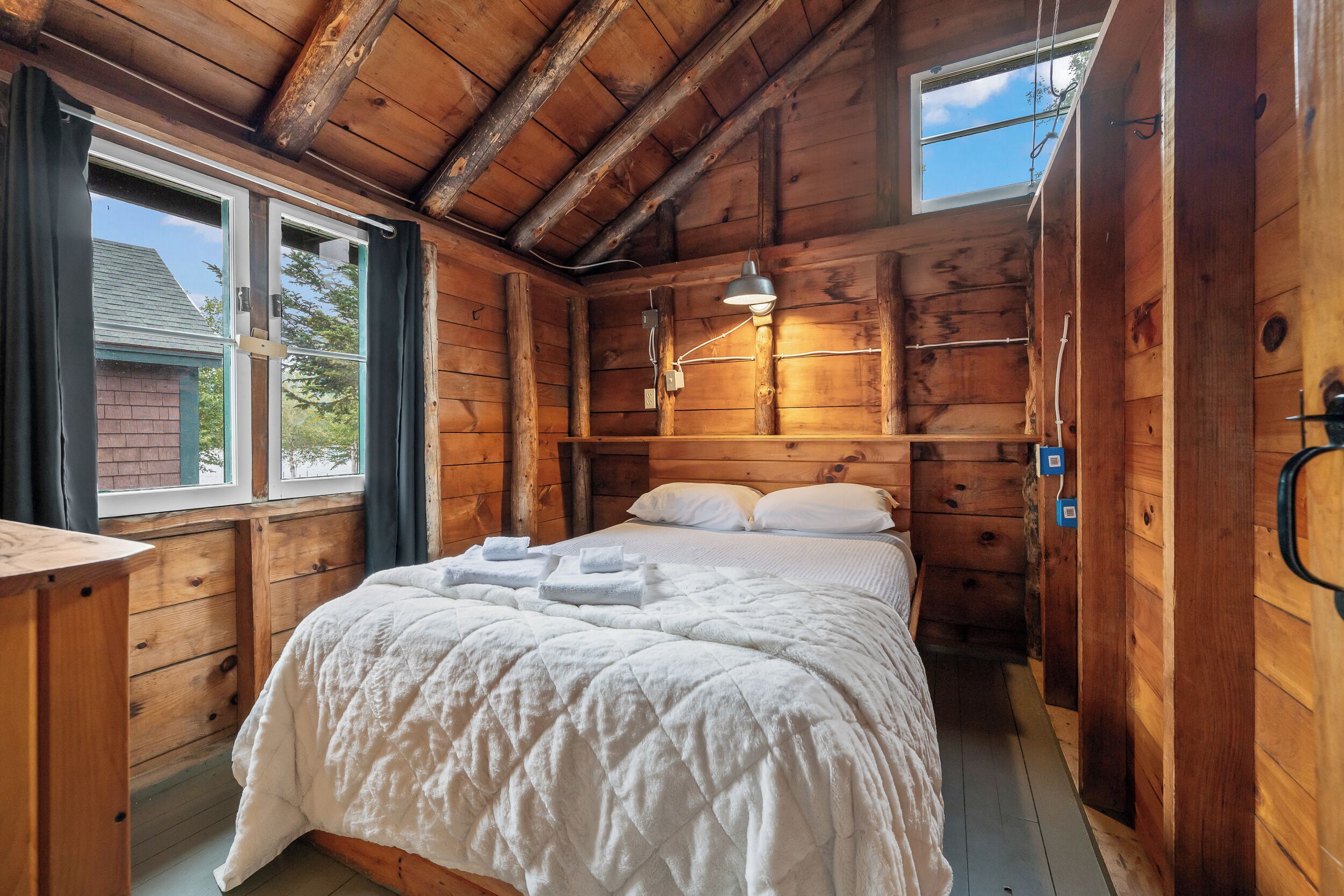 A wooden cabin bedroom with a bed, a desk, and a window.