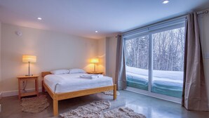 Ett modernt sovrum med en stor säng, två sängbord med lampor, en mjuk matta och ett stort fönster med utsikt över ett snötäckt landskap.