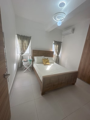 Une chambre à coucher avec un lit en bois, des rideaux blancs, une petite table de chevet et un luminaire fixé au plafond.
