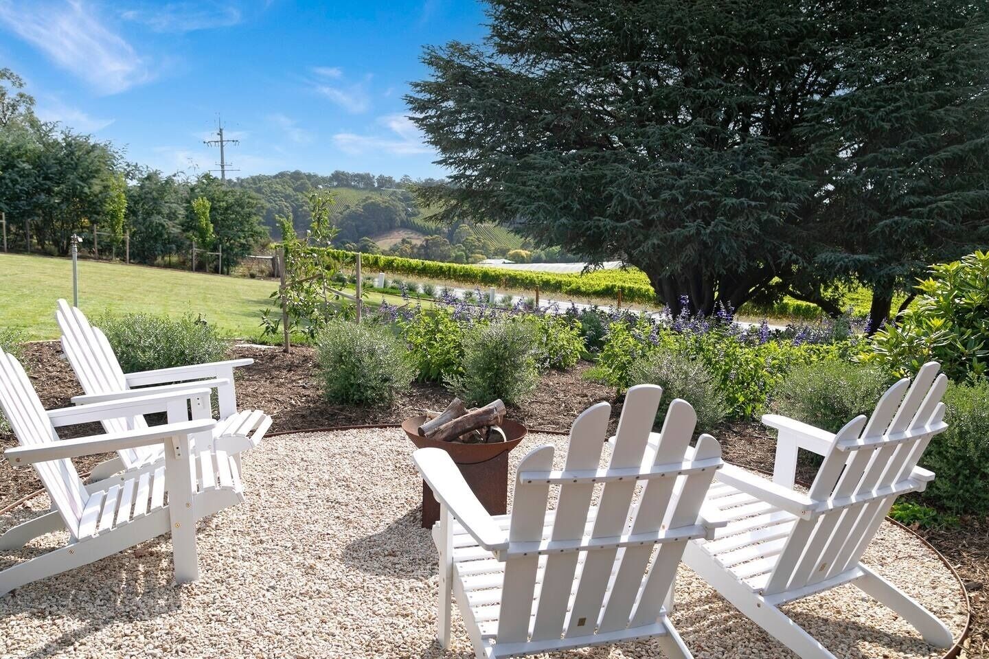 A garden with Adirondack chairs, a fire pit, and a view of a vineyard.