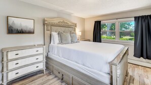 A bedroom with a bed, a dresser, a nightstand, and a window with curtains.