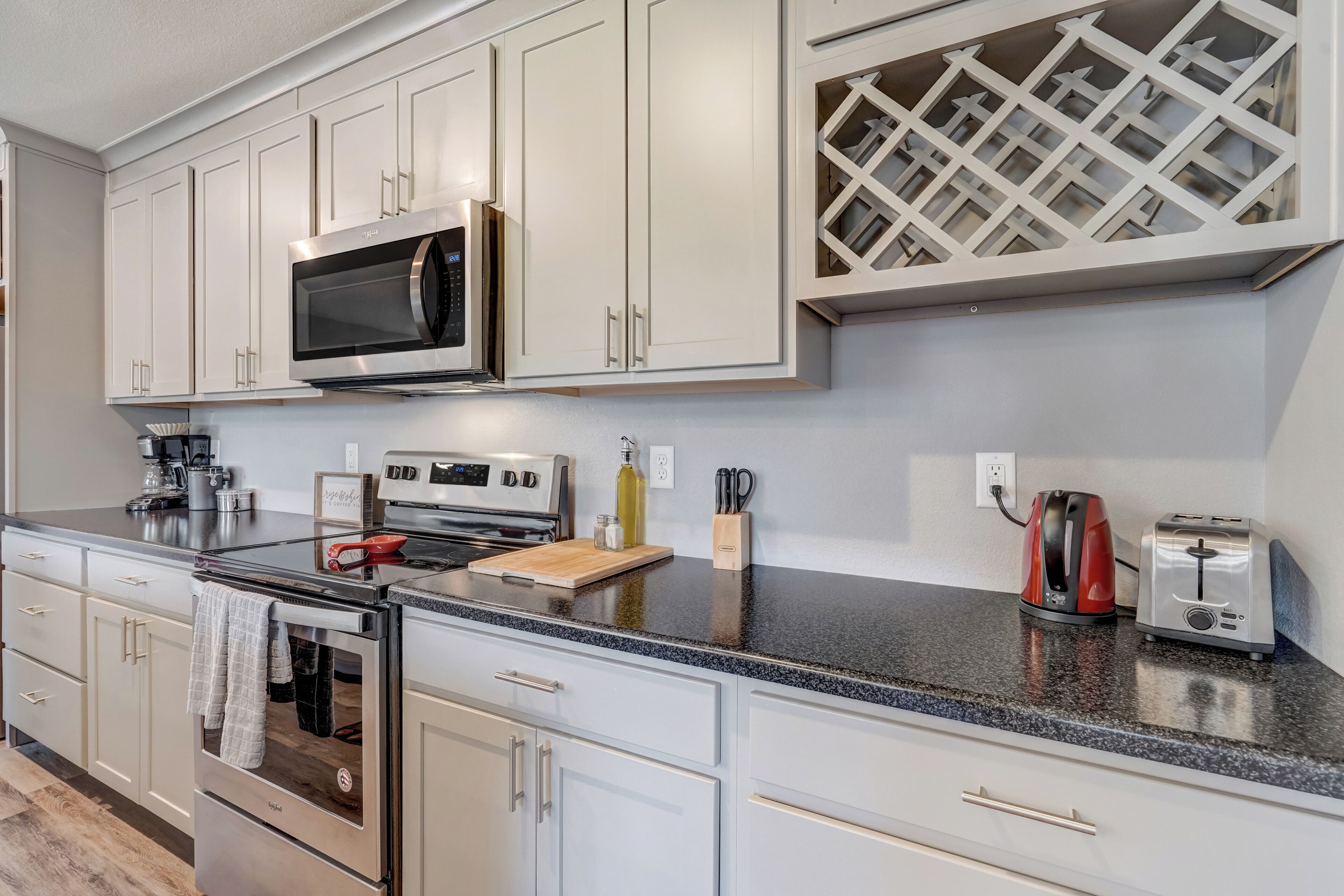A modern kitchen with white cabinetry, stainless steel appliances, a granite countertop, and a wine rack.