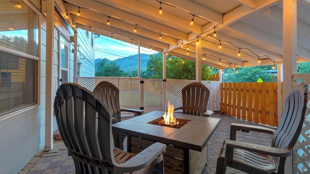An outdoor patio with a fire table, chairs, string lights, and a view of mountains.
