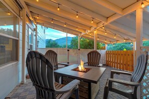 An outdoor patio with a fire table, chairs, string lights, and a view of mountains. - OCC Complex (Colorado Springs)