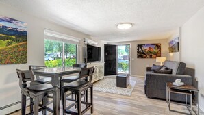 A modern living room with a dining area, a grey sofa, a TV, and artwork on the walls.