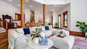 Un salón espacioso con un sofá modular grande, columnas de madera y un comedor al fondo.