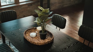 A dark wooden table with a woven placemat, a potted plant, and a candle. - Large Condo in the heart of GR (Grand Rapids)