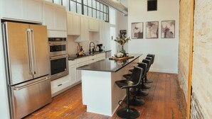 A modern kitchen with stainless steel appliances, a central island with bar stools, and artwork on the walls. - Large Condo in the heart of GR (Grand Rapids)