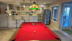 A pool table in a room with a kitchen area, a refrigerator, and a door with blinds. - Calgary Lake House B&B (Calgary)