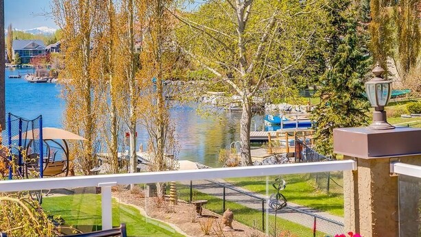 A lakeside view from a balcony with a view of a dock, trees, and a building in the background. - Calgary Lake House B&B (Calgary)