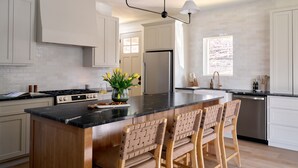 Een moderne keuken met een centraal eiland, houten stoelen, een fornuis en een koelkast.