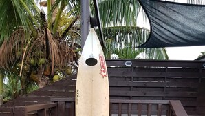 Une planche de surf suspendue à une barrière, avec une clôture en bois et des palmiers en arrière-plan.
