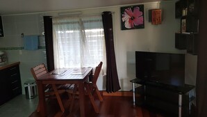 Un coin repas avec une table et des chaises en bois, un téléviseur et une fenêtre avec des rideaux.