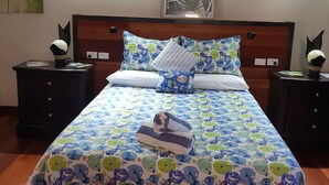 Un lit bien fait, recouvert d’une couvre-lit à motifs floraux, avec deux oreillers et une serviette pliée posée sur un plancher en bois.