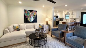 A modern living room with a sofa, armchairs, a coffee table, and a kitchen in the background.