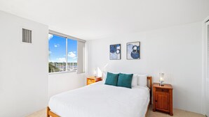 A bedroom with a large bed, two nightstands, a window with a view, and two wall-mounted artworks.