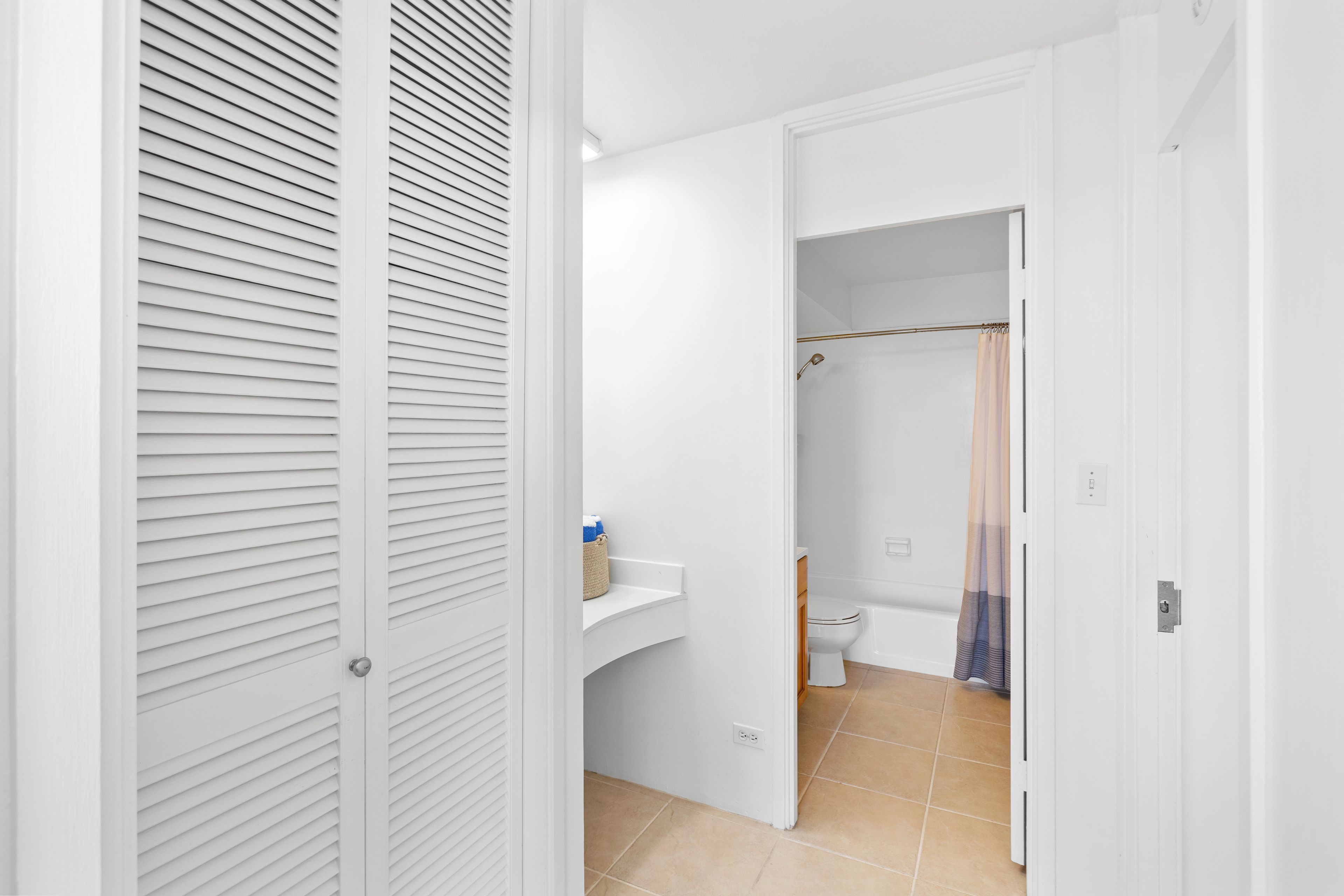 A hallway leading to a bathroom with a toilet, sink, and shower area.