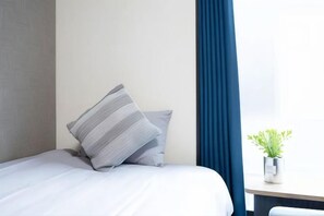 A hotel room with a bed, a bedside table with a plant, and a window with blue curtains. - Shishinkaku (Kyoto)