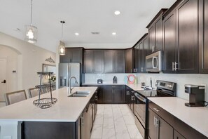 A modern kitchen with dark cabinets, stainless steel appliances, and a central island with a light-colored countertop. - 8966CCD: Stunning ChampionsGate 6bd with Pool (Davenport)