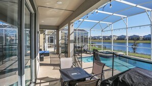 A covered outdoor area with a pool, lounge chairs, and a table. - 8966CCD: Stunning ChampionsGate 6bd with Pool (Davenport)