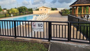 A swimming pool with a 'No Eating or Drinking at Pool Side' sign, surrounded by a fence, with a gazebo and a building in the background. - Charming family home in a serene gated community of The Crossings (The Crossings)