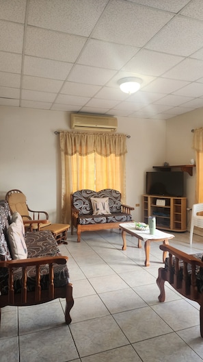 Un salon comprenant un canapé, des fauteuils, une table basse, un téléviseur et un appareil de climatisation.