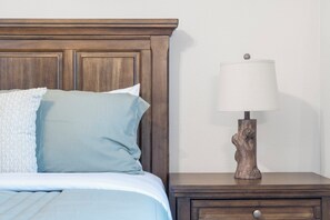 Una cama con cabecera, una lámpara de mesita de noche y una mesita auxiliar.