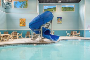 Una piscina interior con un tobogán azul, sillas de descanso y obras de arte en las paredes.