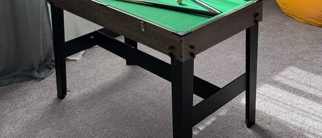 A pool table with a green felt surface, two pool cues, and a set of balls.