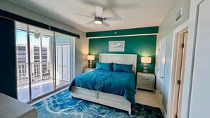 Une chambre à coucher comprenant un lit, deux tables de chevet, un ventilateur de plafond et une vue sur l’extérieur grâce à une porte coulissante.