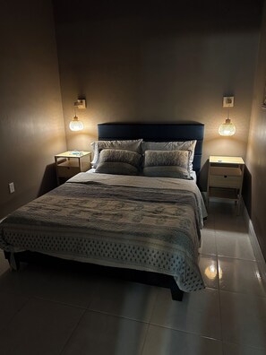 A neatly made bed with a patterned bedspread and pillows, flanked by two bedside tables with lamps, in a room with plain walls and a tiled floor. - EXTRAORDINARY EXPERIENCE 3/broom 2/bath house in lovely Windermere with WiFi, AC (Windermere)