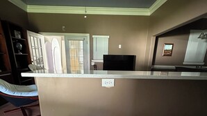 Una cocina moderna con una isla central, dos taburetes de bar, un ventilador de techo y un televisor.