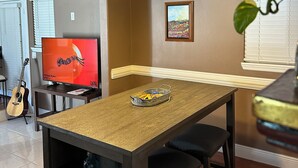 Un comedor con una mesa de madera, sillas, una lámpara colgante, un televisor y una planta.