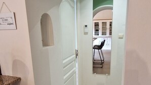 Um corredor com chão de madeira, uma área de cozinha com armários e uma cadeira, e um aviso na parede.