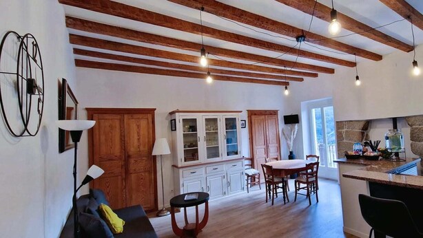 Cozinha espaçosa com vigas de madeira, área de jantar com mesa e cadeiras, e um balcão com parede de pedra e um grande dispensador de água.