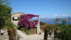 Una casa de piedra con un sendero de piedra que lleva a una puerta de madera, rodeada de vegetación exuberante y flores coloridas.