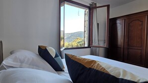 Una habitación de hotel con una cama, un ventanal con vistas a las montañas y un armario de madera.
