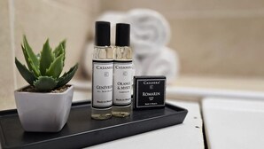 Una encimera de baño con una planta de aloe vera en maceta, dos botellas de champú Casanera de naranja y mirto, y una caja de jabón Casanera Romarin.