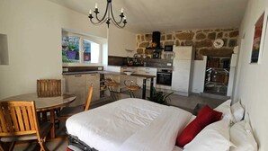Un dormitorio con cama, una mesa de comedor con sillas, una kitchenette y una pared de piedra.