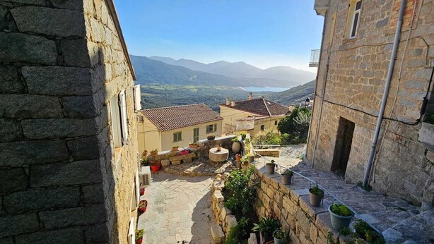 Un patio estrecho con muros de piedra, plantas en macetas y vistas a montañas distantes.