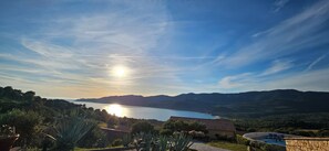 Vista di un lago con montagne sullo sfondo, cielo sereno e un edificio con piscina.