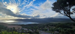 Paesaggio costiero con vista sul mare, montagne e un sentiero alberato.