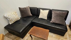 Un sofá seccional de cuero negro con tres cojines, uno con un estampado de lunares blancos y dorados, y una pequeña mesa de centro de madera al frente.
