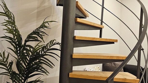 Una escalera de caracol con escalones de madera y barandillas de metal negro.