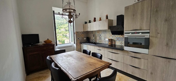 A modern kitchen with a wooden table and chairs, a built-in oven, and a window with a view of greenery. - Beautiful & old renovated T3 apartment in Sartène (Sartène)