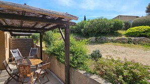 A patio with a wooden table and chairs, a pergola, and a garden with various plants and a rock formation. - Mini Caseddu T2, Pool & sea view, Alba Rossa N°11 (Serra-di-Ferro)