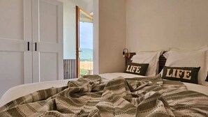 A bedroom with a bed, two pillows with the word "LIFE" on them, a striped blanket, and a view of the outdoors through a door. - Mini Caseddu T2, Pool & sea view, Alba Rossa N°11 (Serra-di-Ferro)