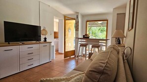 A compact living space with a kitchenette, a sofa, a TV, and a dining area with a view of greenery. - Mini Caseddu T2, Pool & sea view, Alba Rossa N°11 (Serra-di-Ferro)