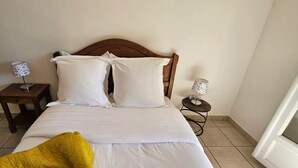 A bedroom with a wooden headboard, a bed with white bedding, two bedside tables with lamps, and a yellow throw blanket on the bed.